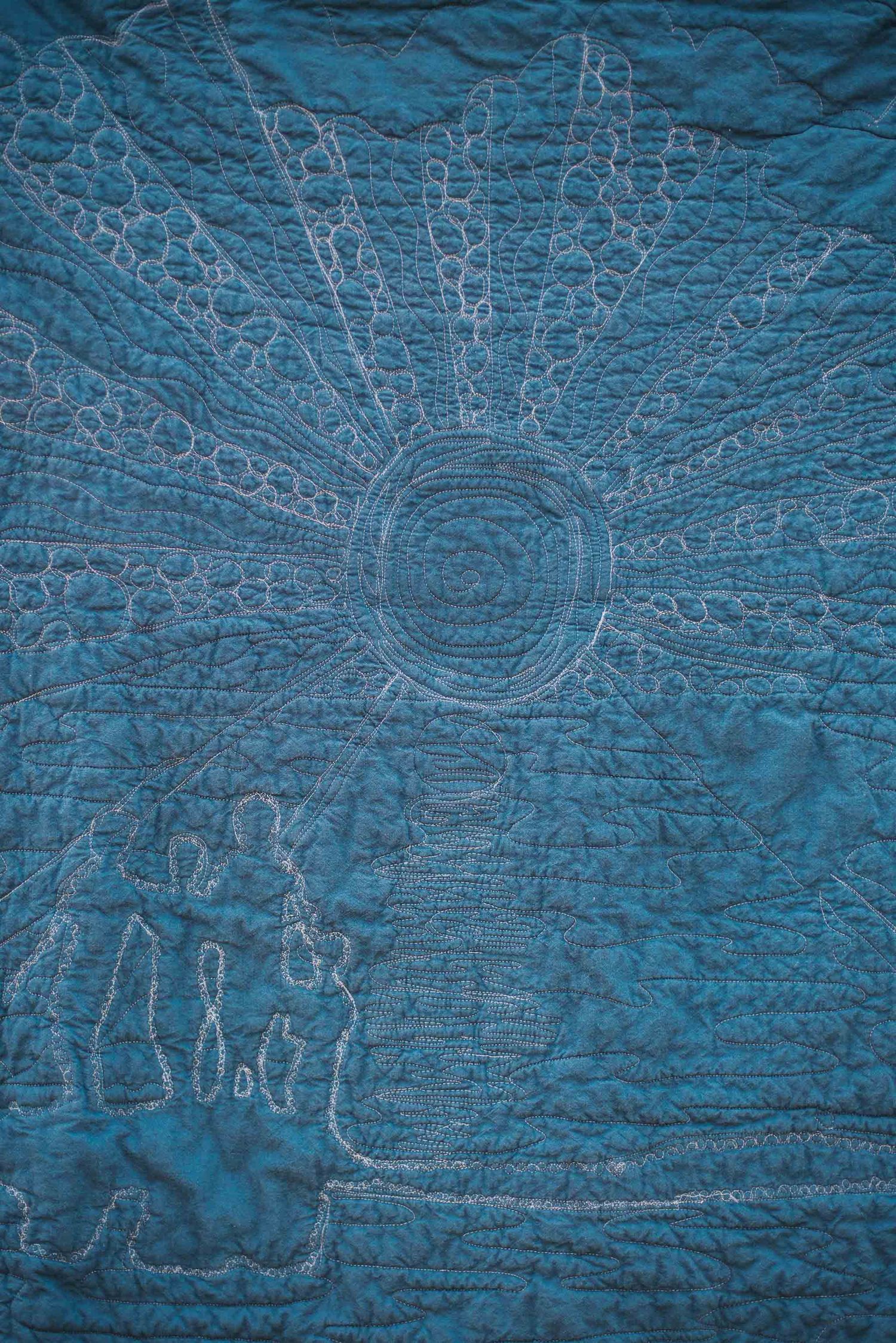 Back of a memory quilt showcasing the free motion quilting of a group of children in the setting sun's rays.