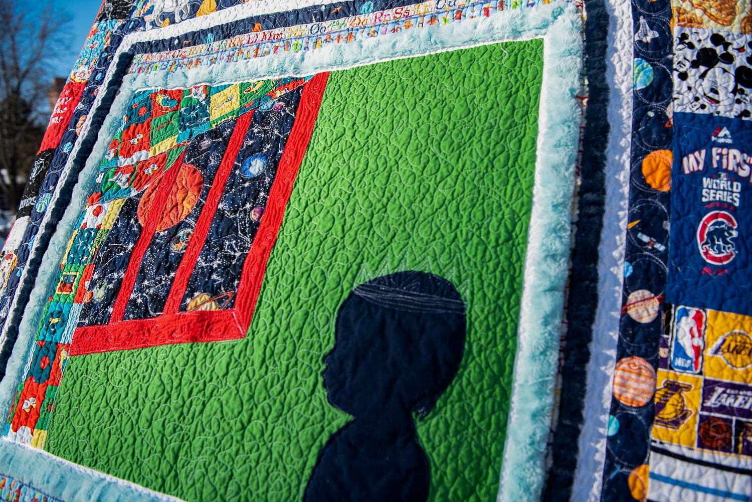 Art quilt based on Goodnight Moon with the silhouette of a boy looking out a window to the galaxy.