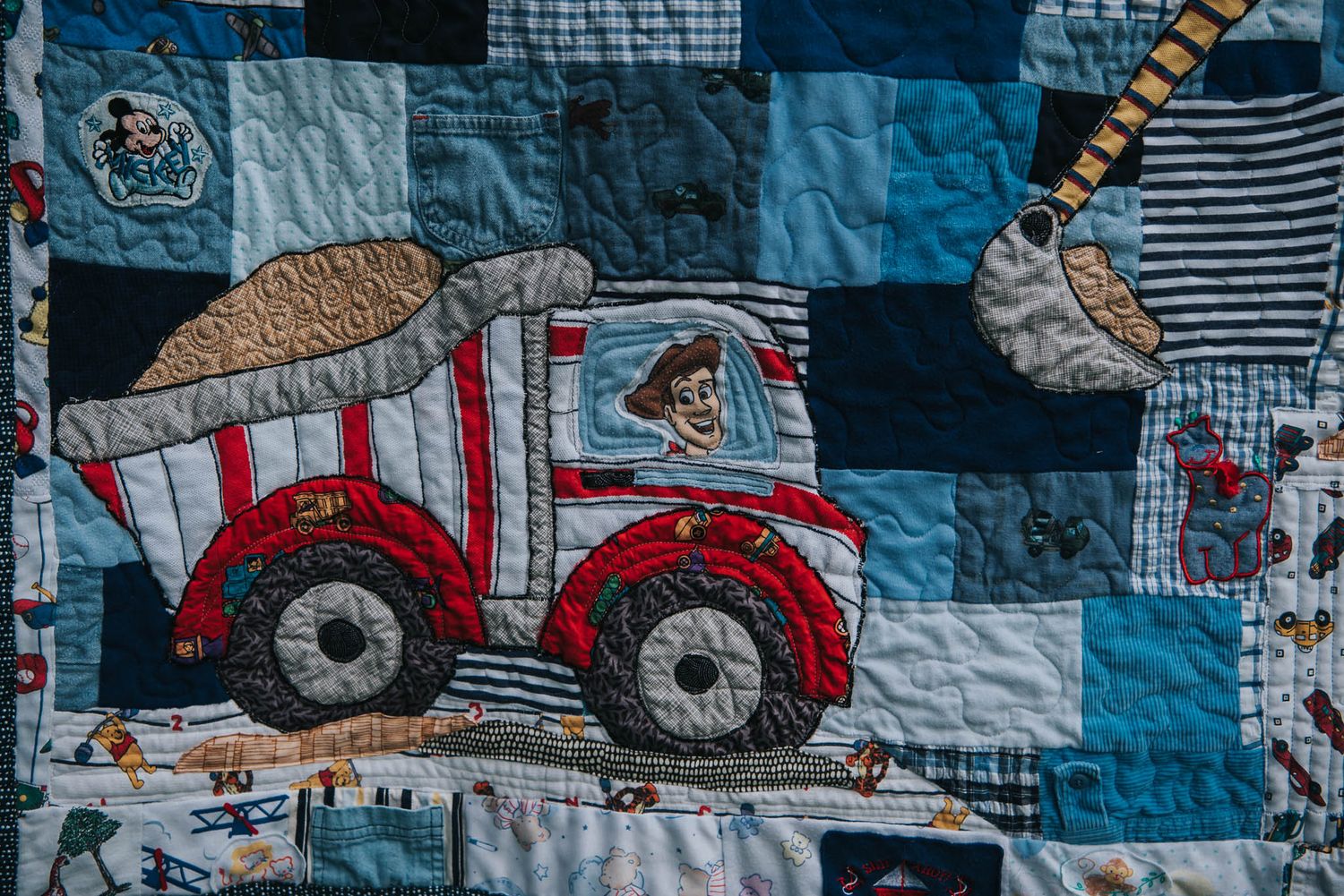 Applique made from baby clothes of a dump truck driven by Woody from Toy Story in a Construction themed memory quilt.