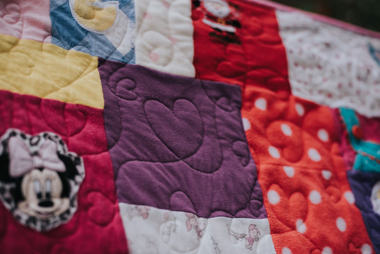 Patchwork memory quilt with a purple square showing stitching in the pattern of a heart.