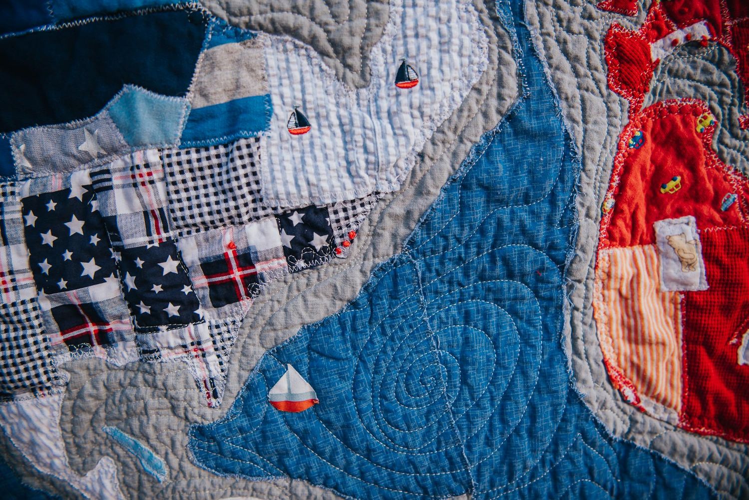 Art quilt featuring a tiny sail boat from an item of clothing and stitching to show water.