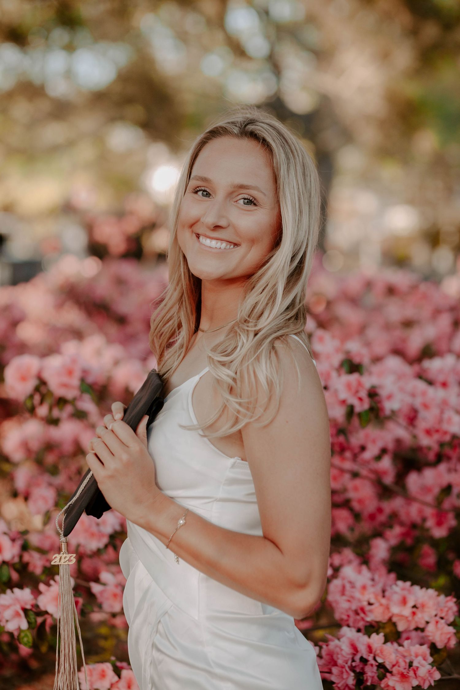Portrait of smiling college graduate in front of pink flowers, taken by Anna Holman.