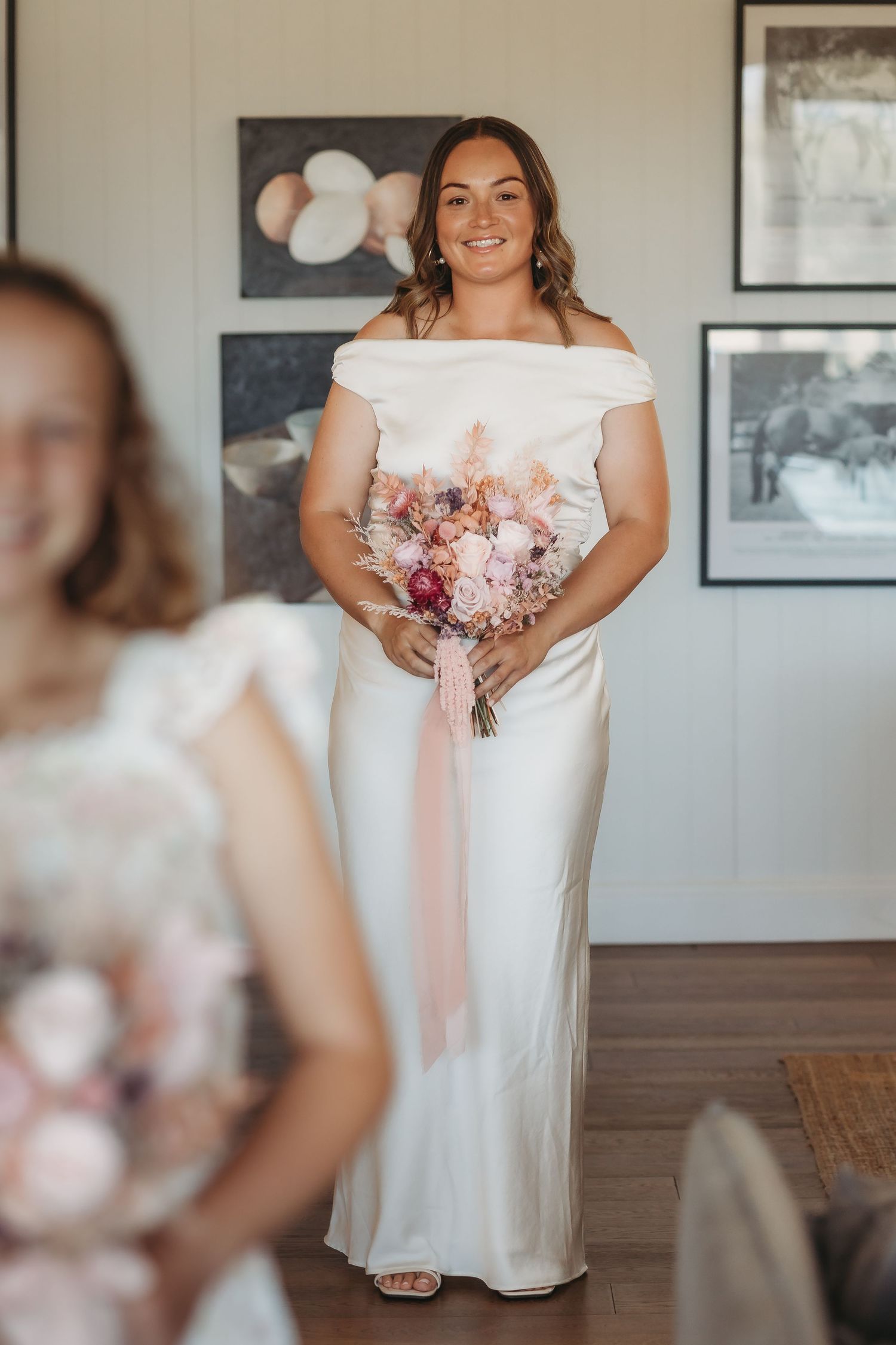 Wedding preparation scene in bright room with framed photos and white dress.