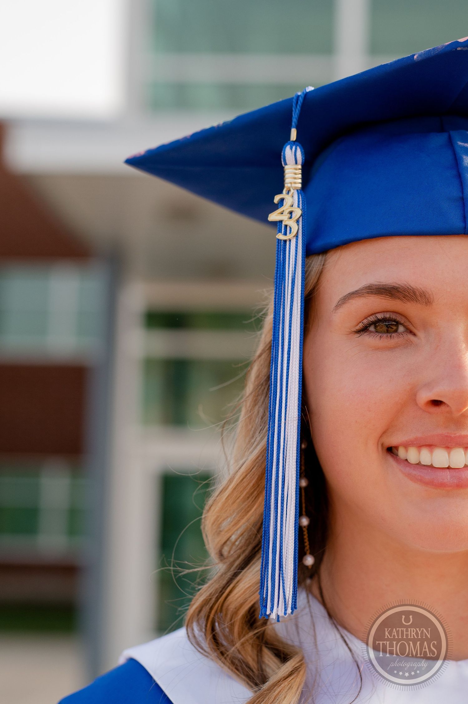 Close-up of graduation cap with blue and silver tassel against school building.