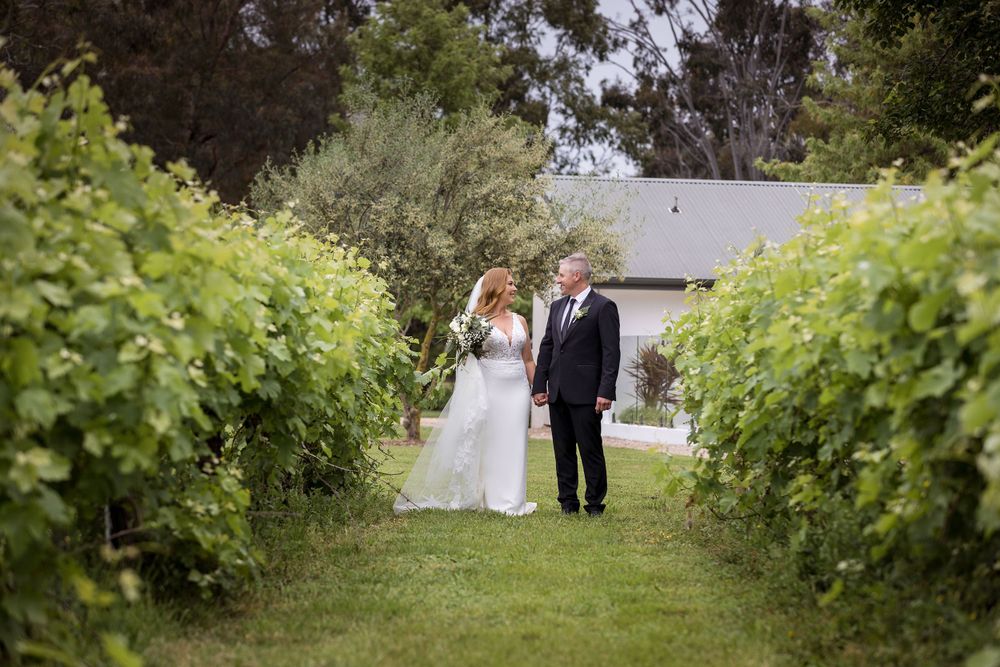 Bride and Groom walking holding hands and sharing a moment in the vines with the Bride holding her wedding flowers