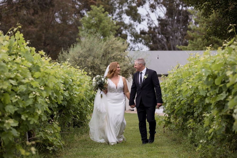 Bride and Groom walking holding hands and sharing a moment in the vines with the Bride holding her wedding flowers