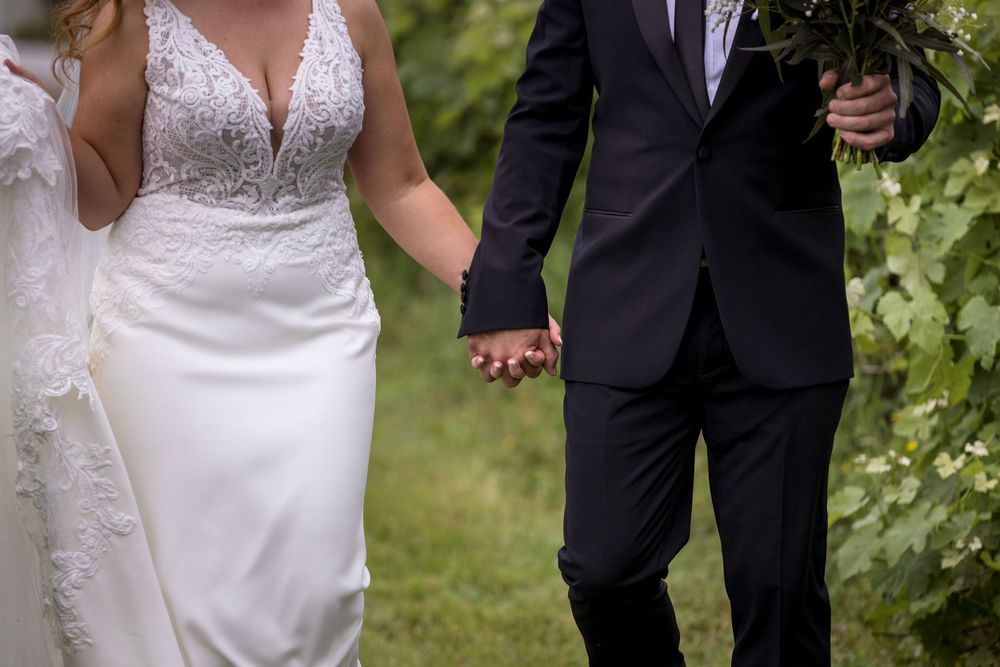 Bride and Groom walking holding hands and sharing a moment in the vines with the groom holding the wedding flowers