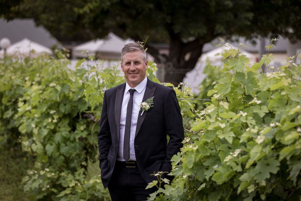Groom in his black suit before his ceremony surrounded by grape vines, captured by Jason Robins Photography.