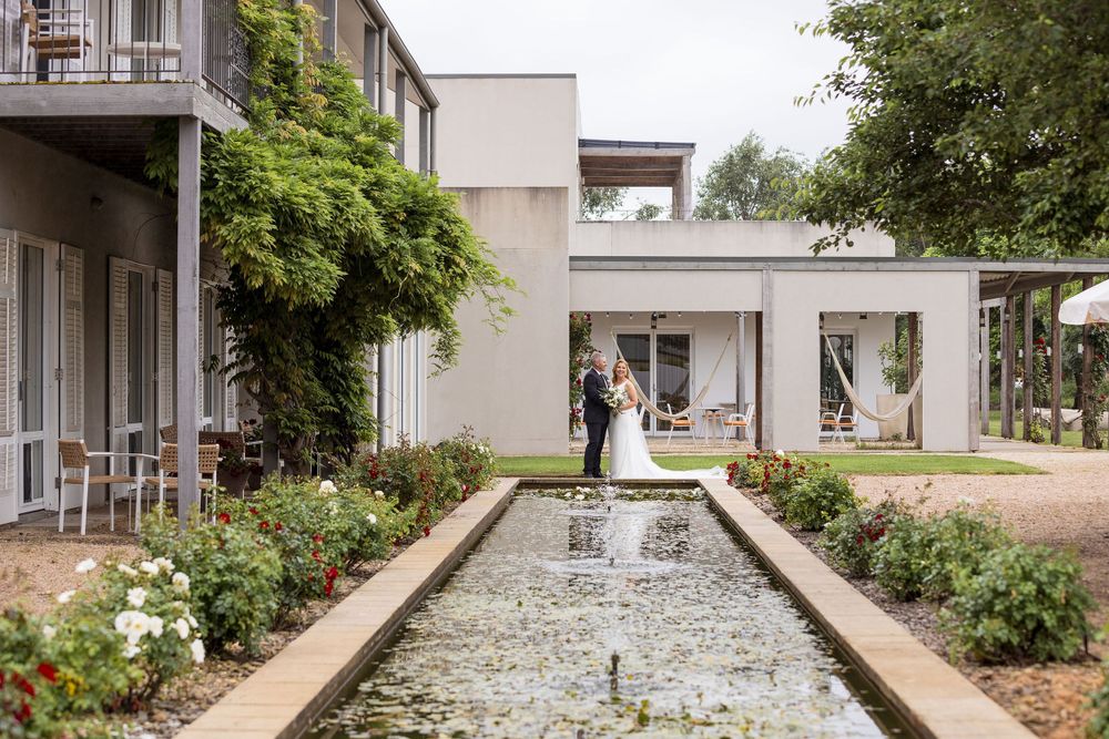 Bride in her wedding dress and the groom in his black suit sharing a moment before their ceremony by the pool.