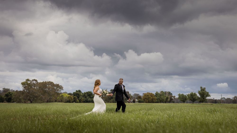 Bride and Groom on their bridal shoot at Brown Brothers Winery, walking holding hands with storm clouds behind them.