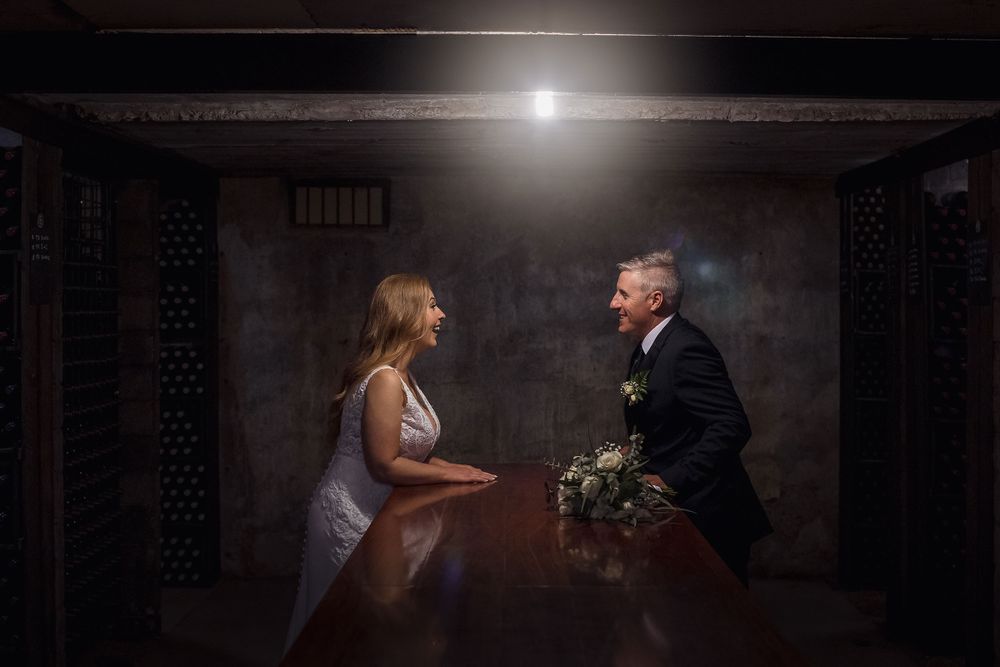 Bride in her white wedding dress and Groom in his black suit, wedding flowers on the table as they share a moment.