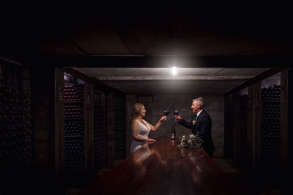 Bride in her white wedding dress and Groom in his black suit, wedding flowers on the table as they share a moment.