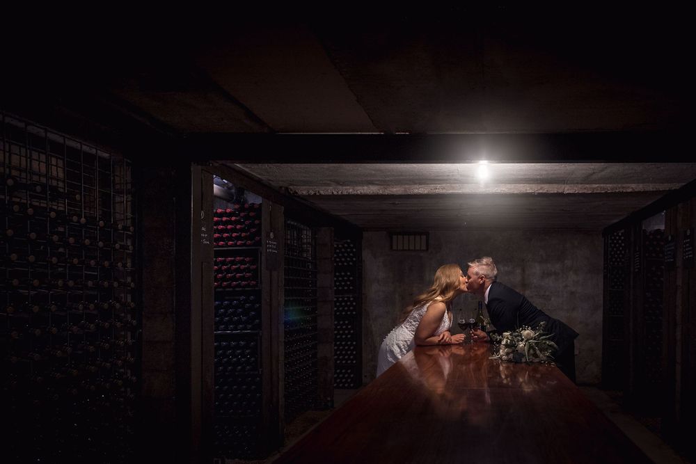 Bride in her white wedding dress and Groom in his black suit, wedding flowers on the table as they share a moment.