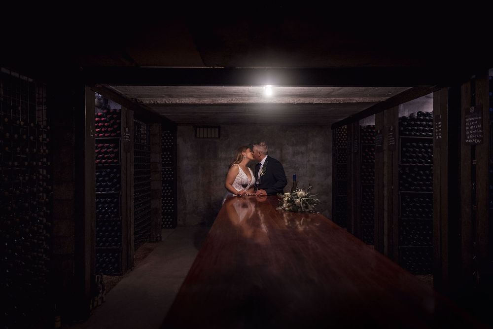 Bride in her white wedding dress and Groom in his black suit, wedding flowers on the table as they share a moment.