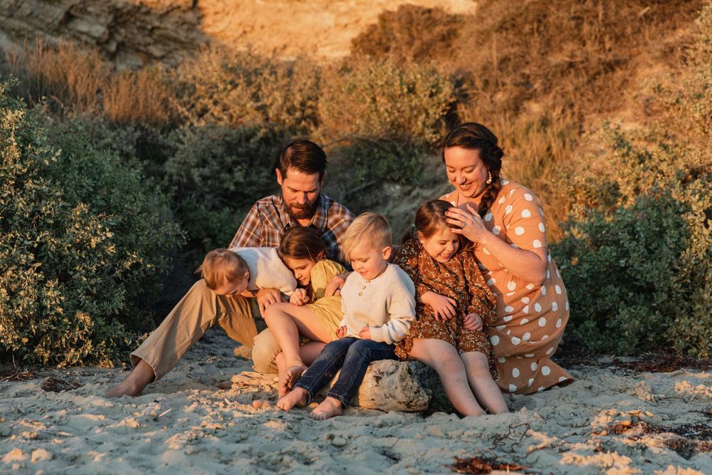 Happy family of six sitting together on sandy beach reading at golden sunset.