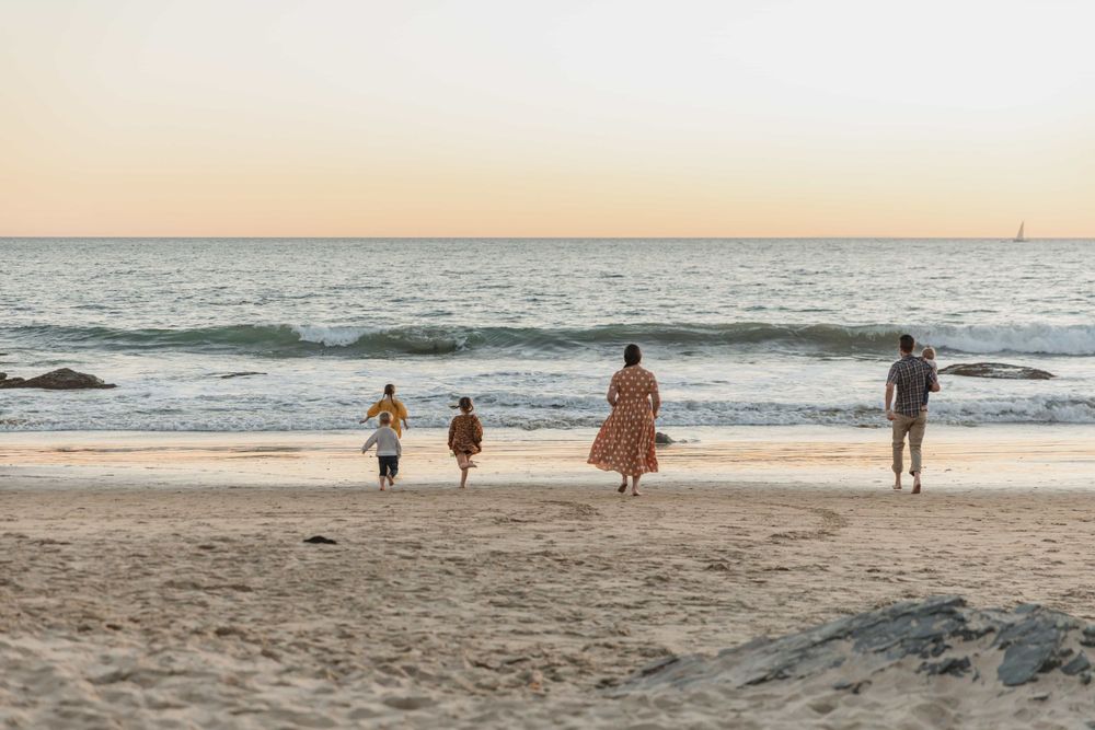 Family walking toward ocean waves on sandy beach at golden sunset.