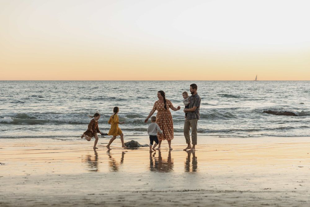 Family playing on a beach at sunset with waves and golden sky.