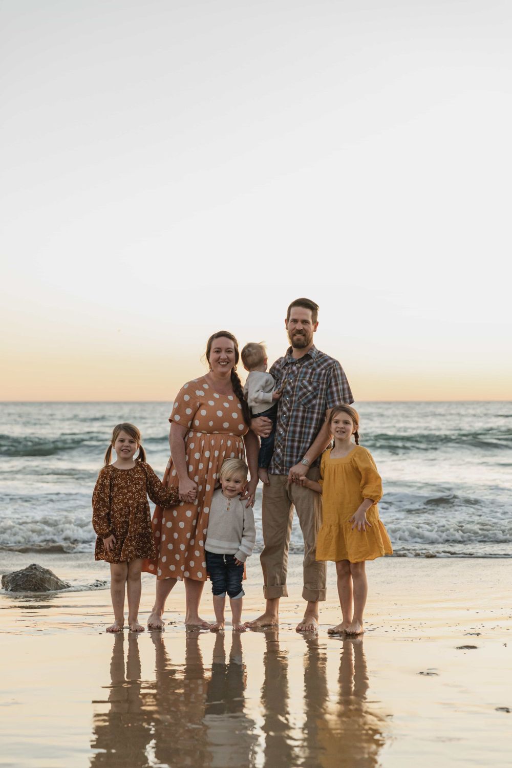 Family of six posing on a wet beach at sunset, smiling warmly.