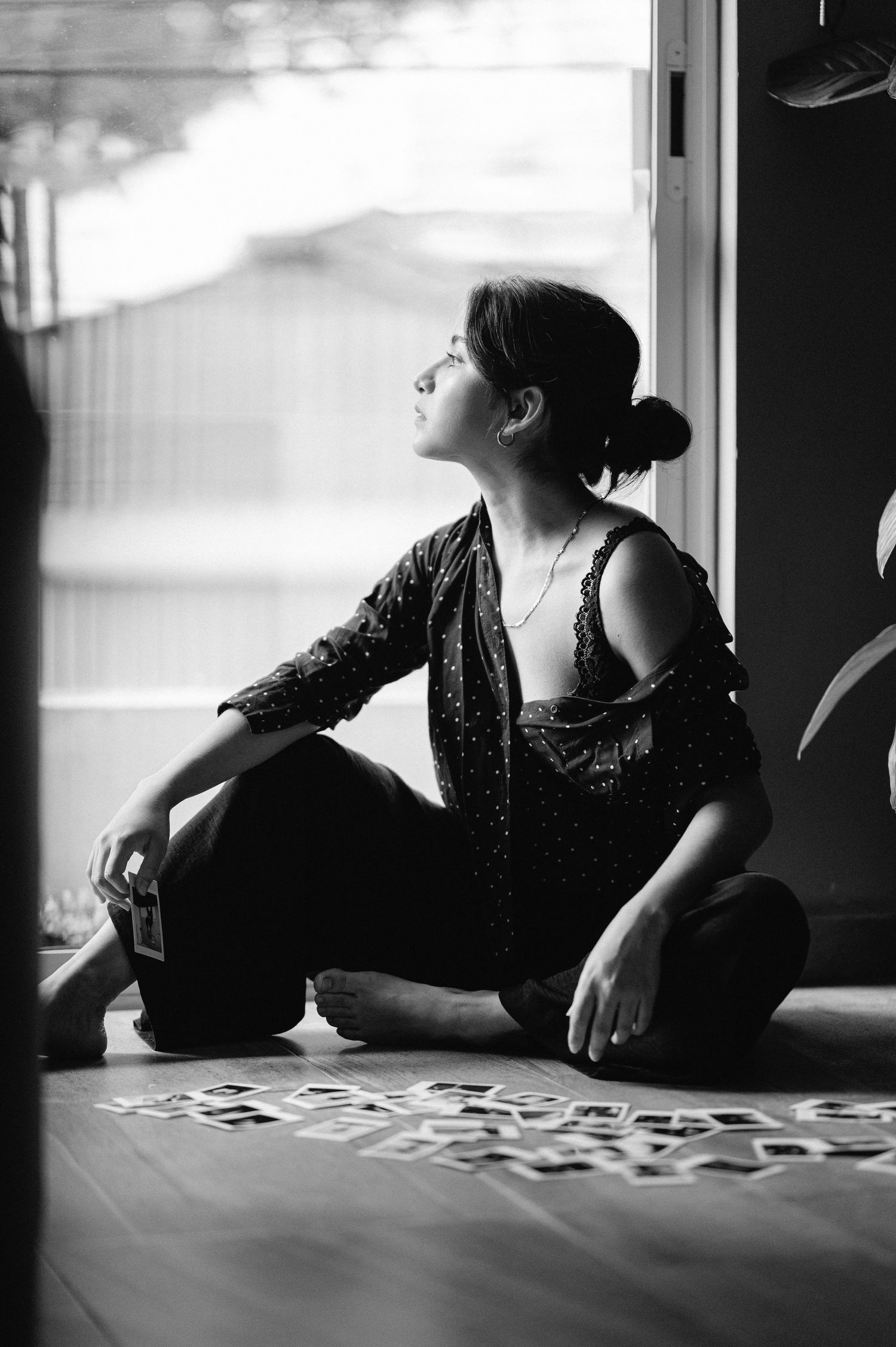 Woman in sparkly dress sitting by window in moody black and white photograph.