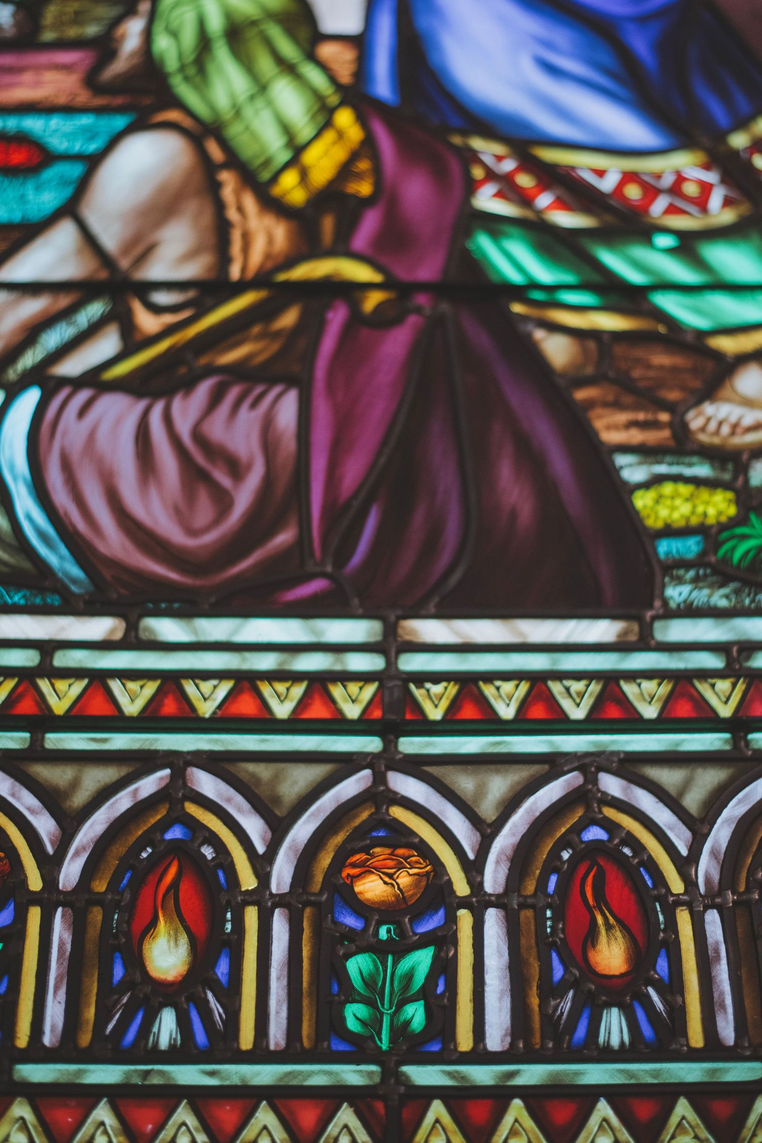 Colorful stained glass window detail showing ornate medieval-style religious artwork and decorative patterns.