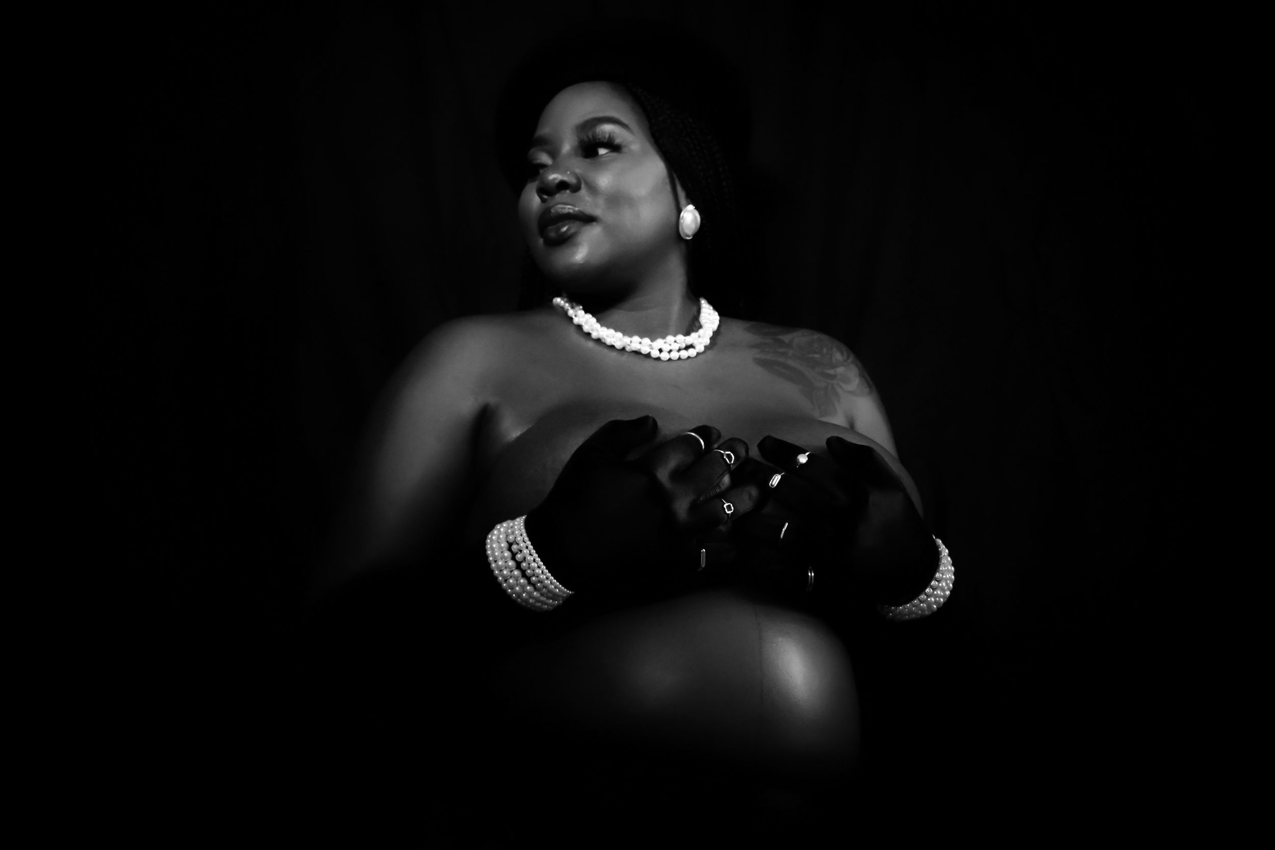 Artistic black and white maternity portrait featuring elegant pearls and gloves against dark background.