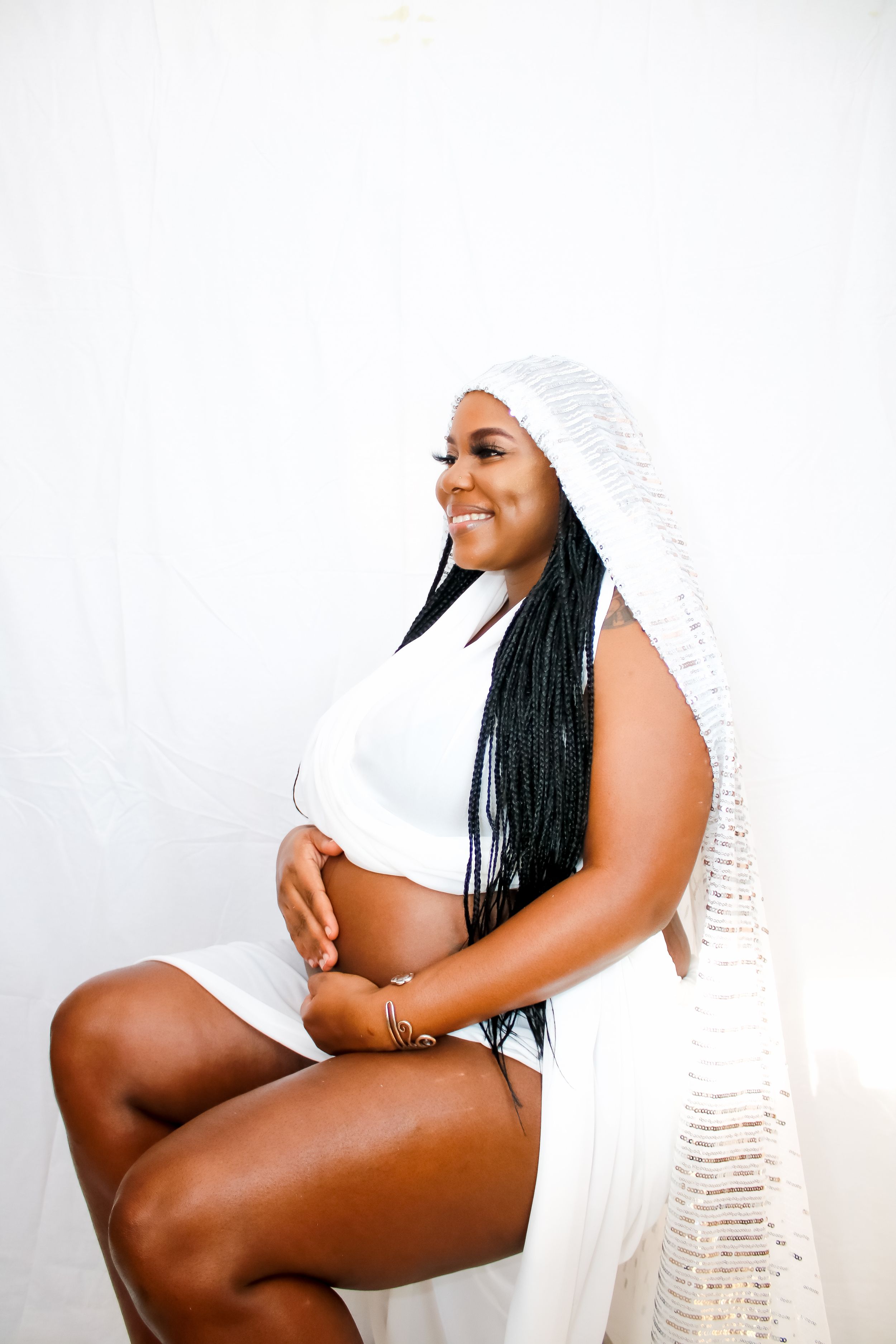 Radiant maternity portrait featuring white crop top and textured fabric wrap with long braids.