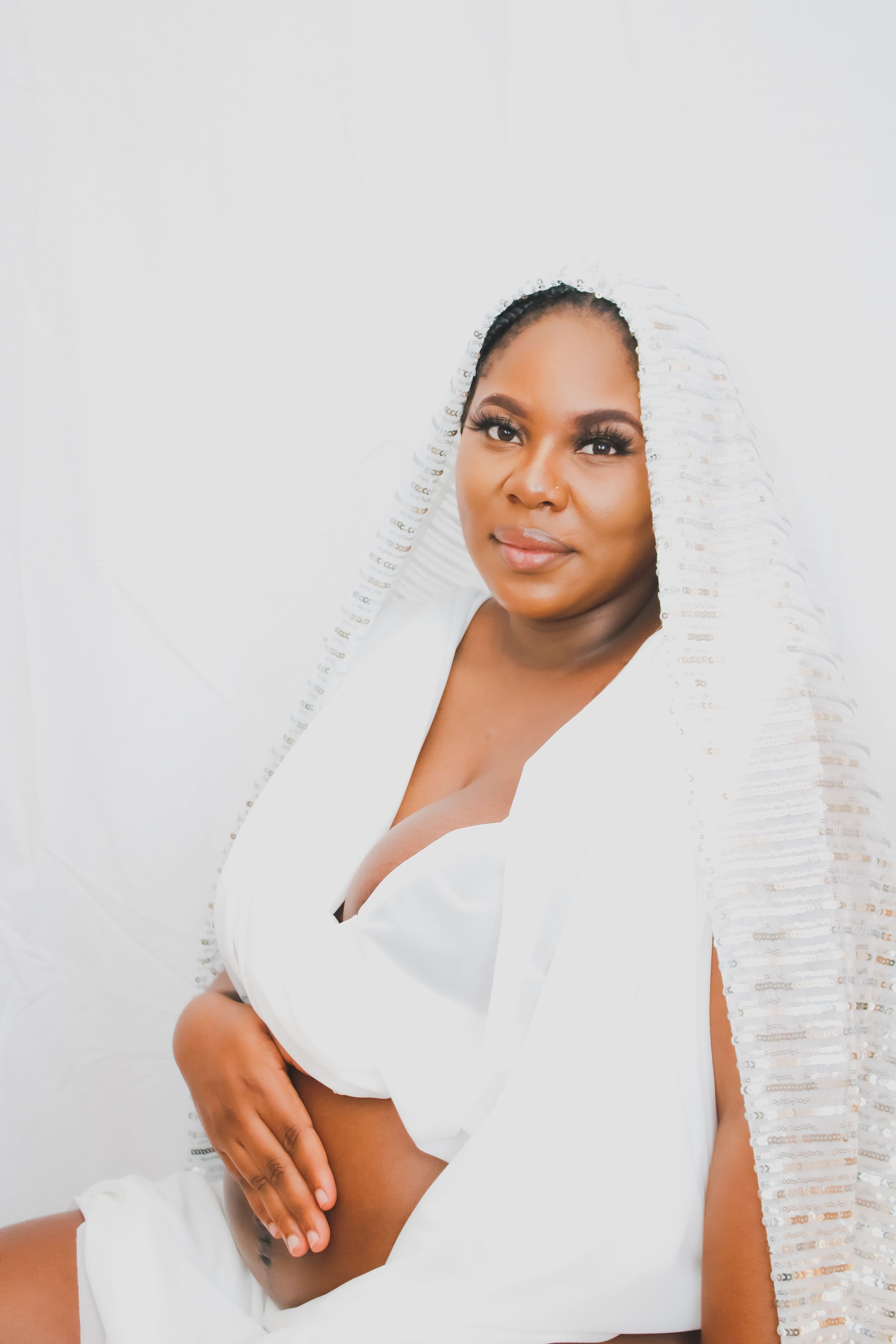 Soft maternity portrait in white attire with delicate veil creating ethereal effect.