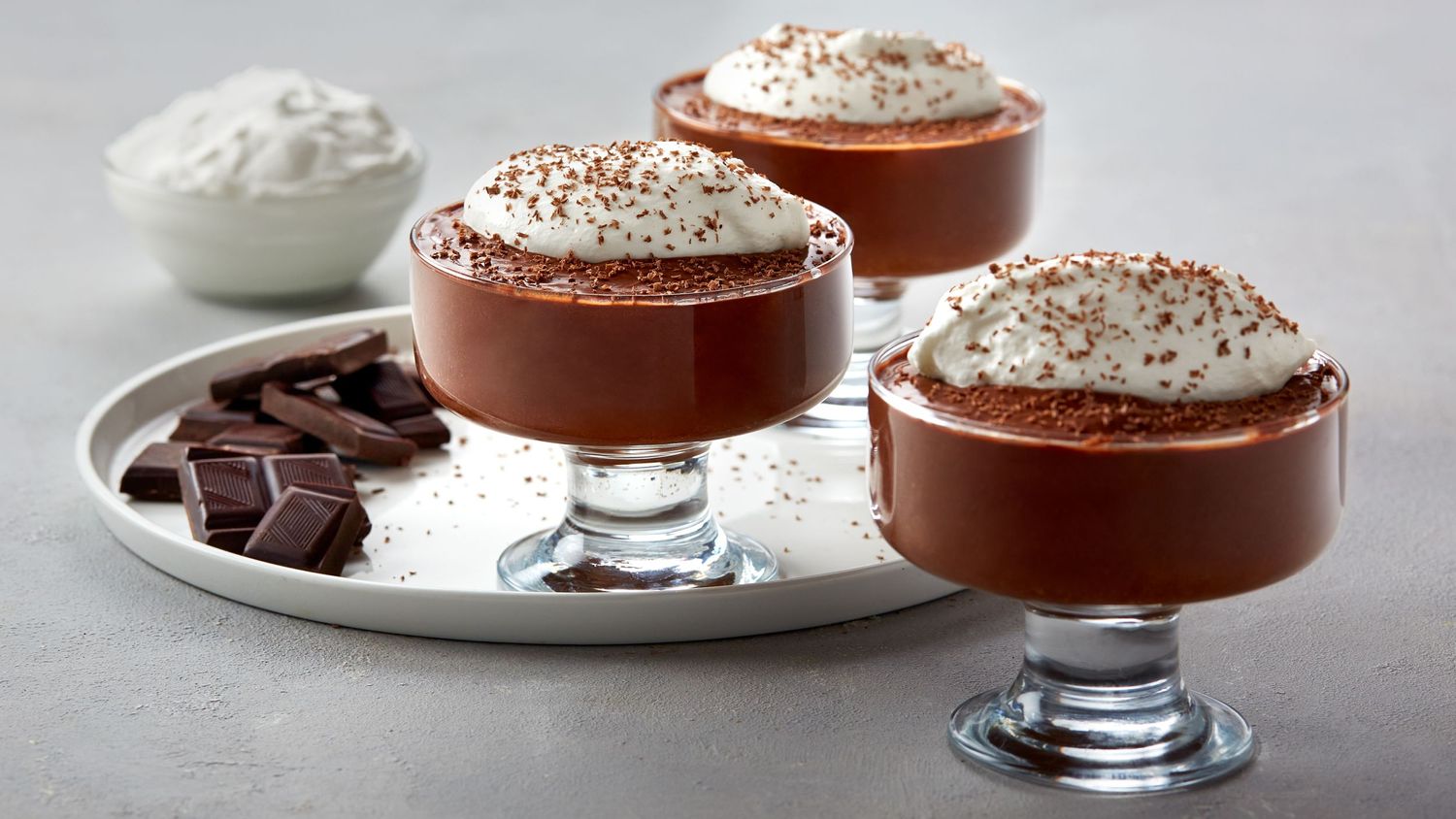 Rich chocolate mousse topped with whipped cream and chocolate shavings served in glass dessert cups.