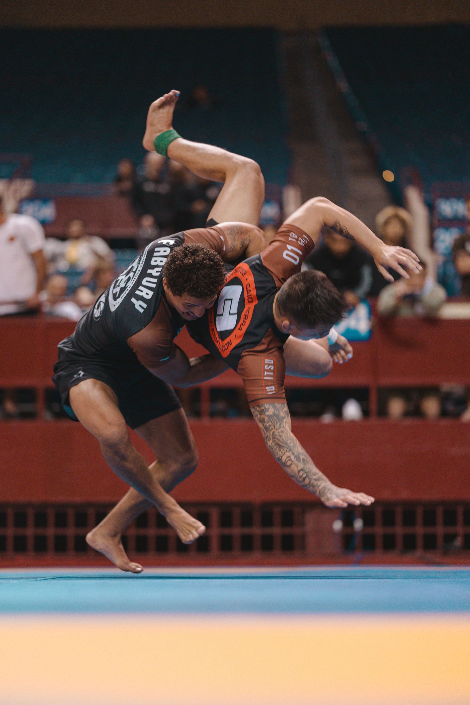 Two Brazilian Jiu-Jitsu competitors engaged in an intense grappling match on a blue competition mat.