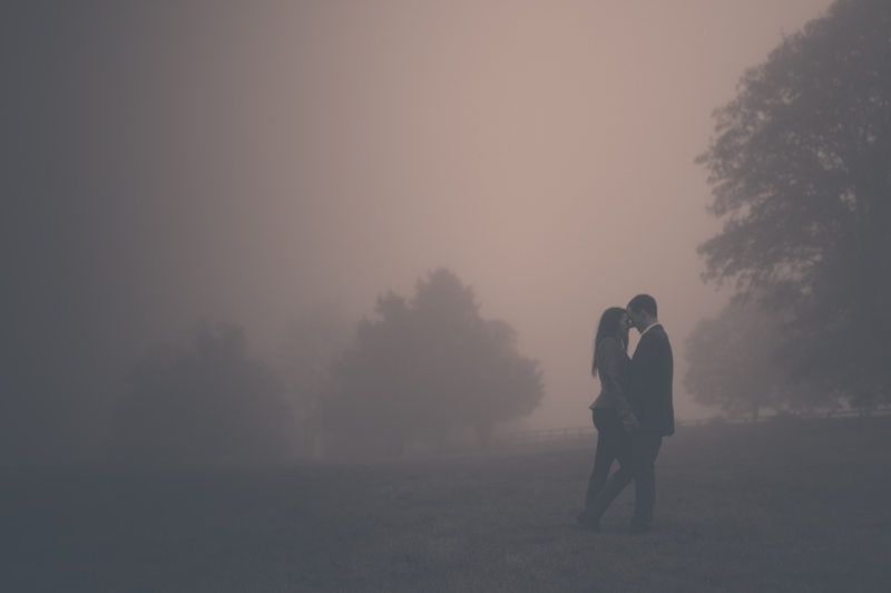 Silhouetted couple embracing in misty foggy field during sunset creates romantic atmosphere.