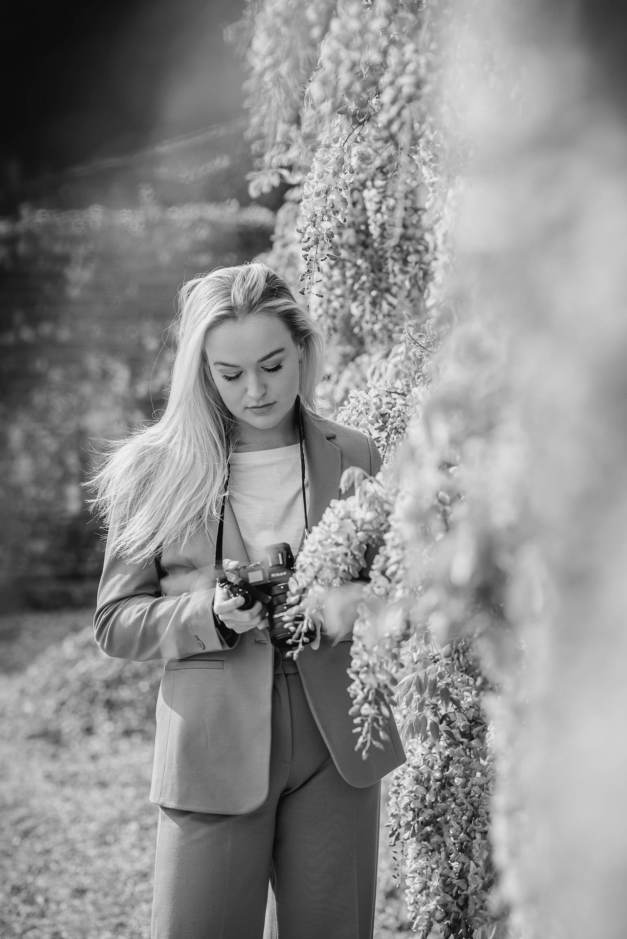 Photographer in beige suit takes photos among hanging wisteria blooms in black and white.