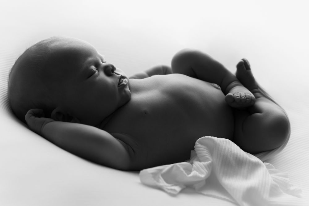 Black and white image of newborn baby girl backlit and silhouetting her features.