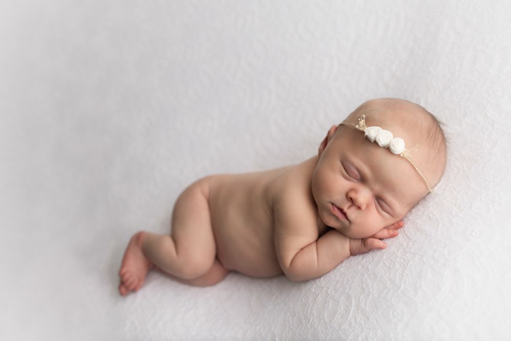 Newborn baby girl laying on her side with her hands under her cheek.