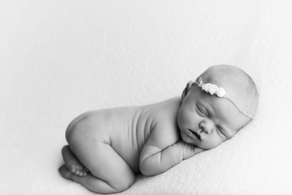 Black and white image of newborn baby girl on her hands and knees sleeping.