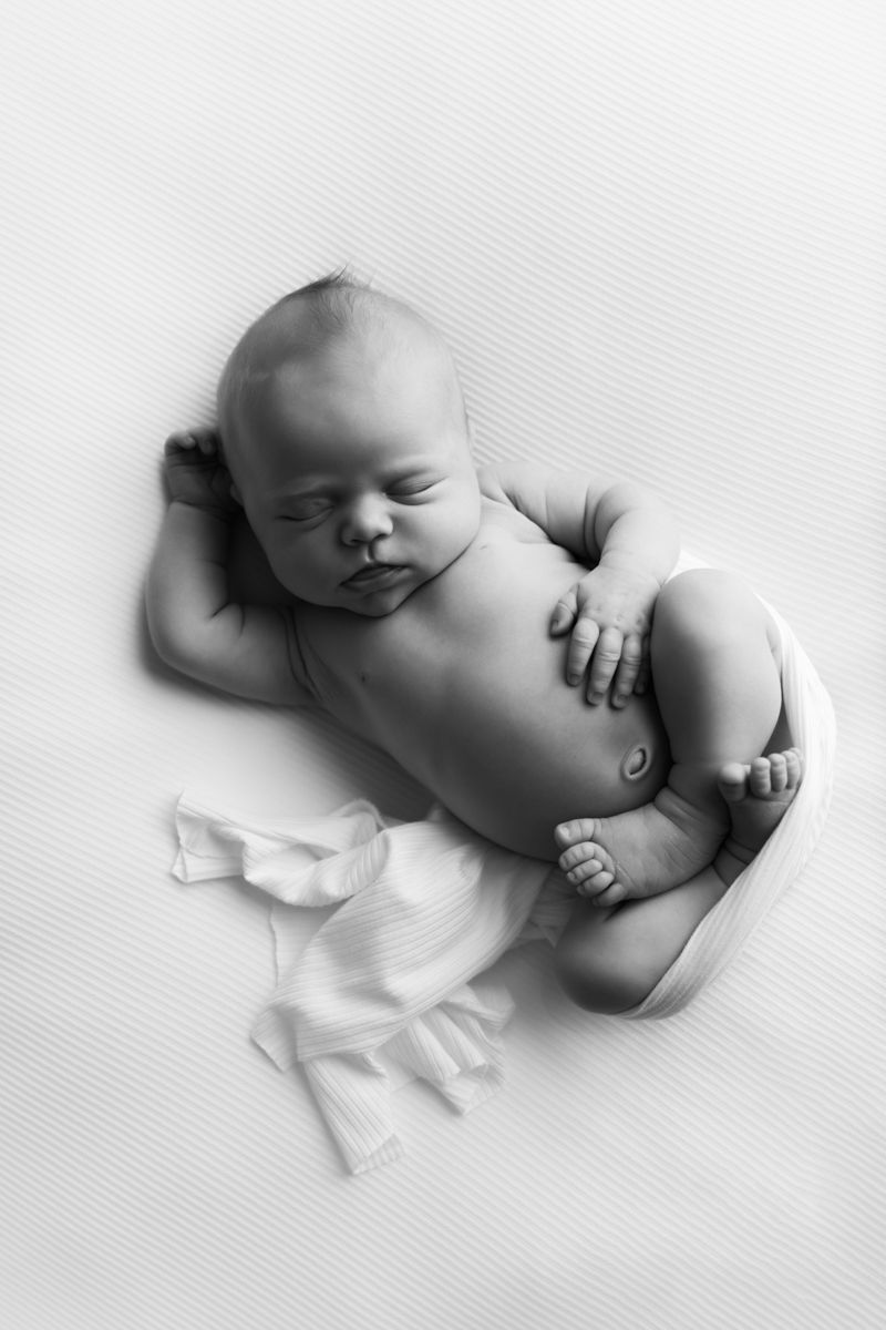 Black and white image of newborn baby girl wrapped and curled into a womb position.