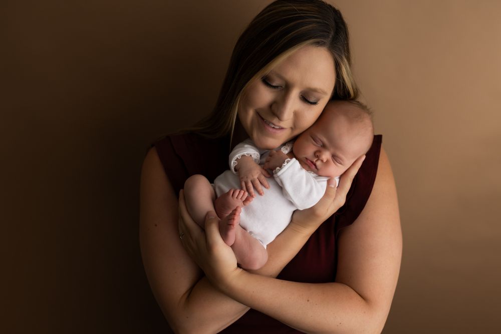 Newborn baby girl being held by her mom.  Her mom is smiling cheek to cheek with baby.