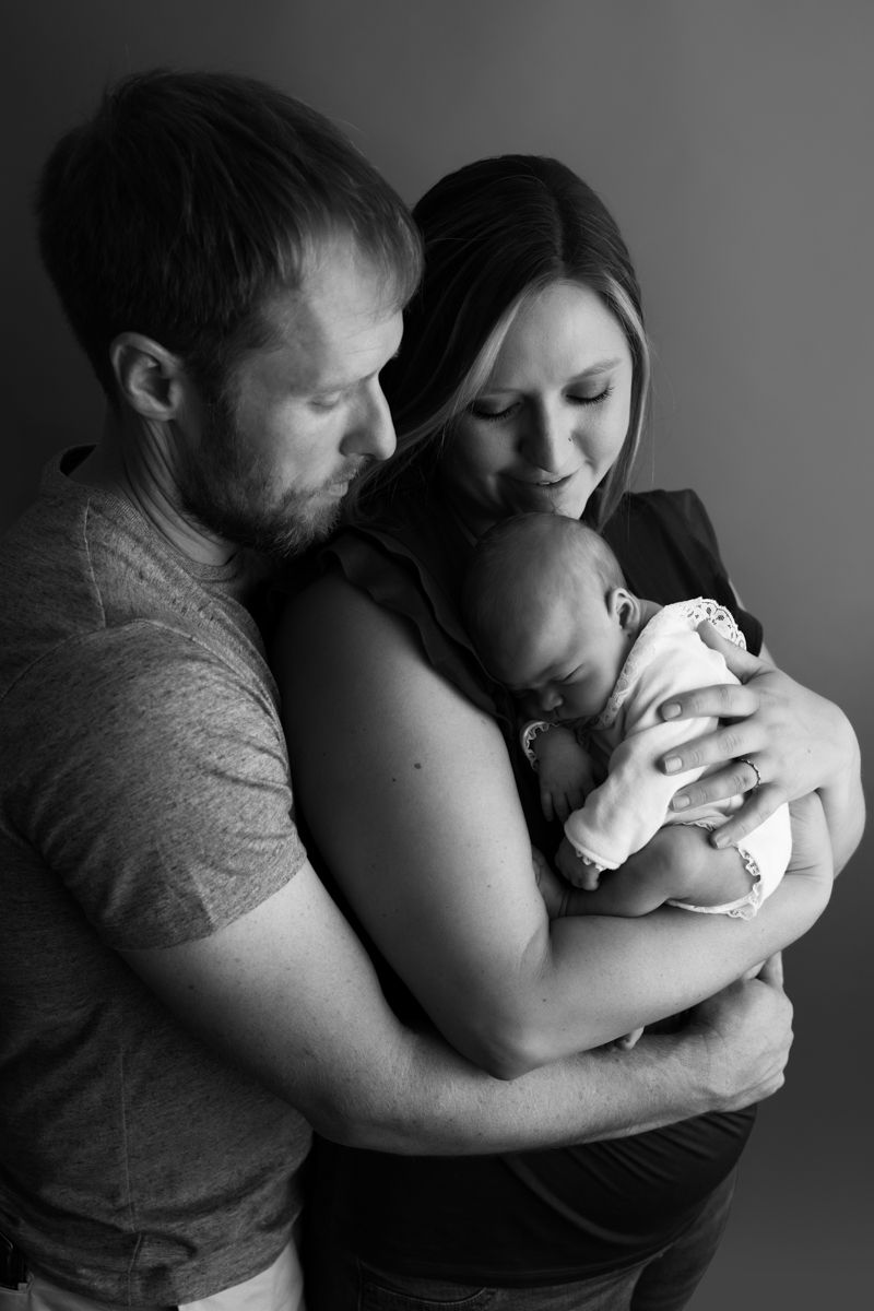 Black and white image of newborn baby girl with mom and dad holding her.