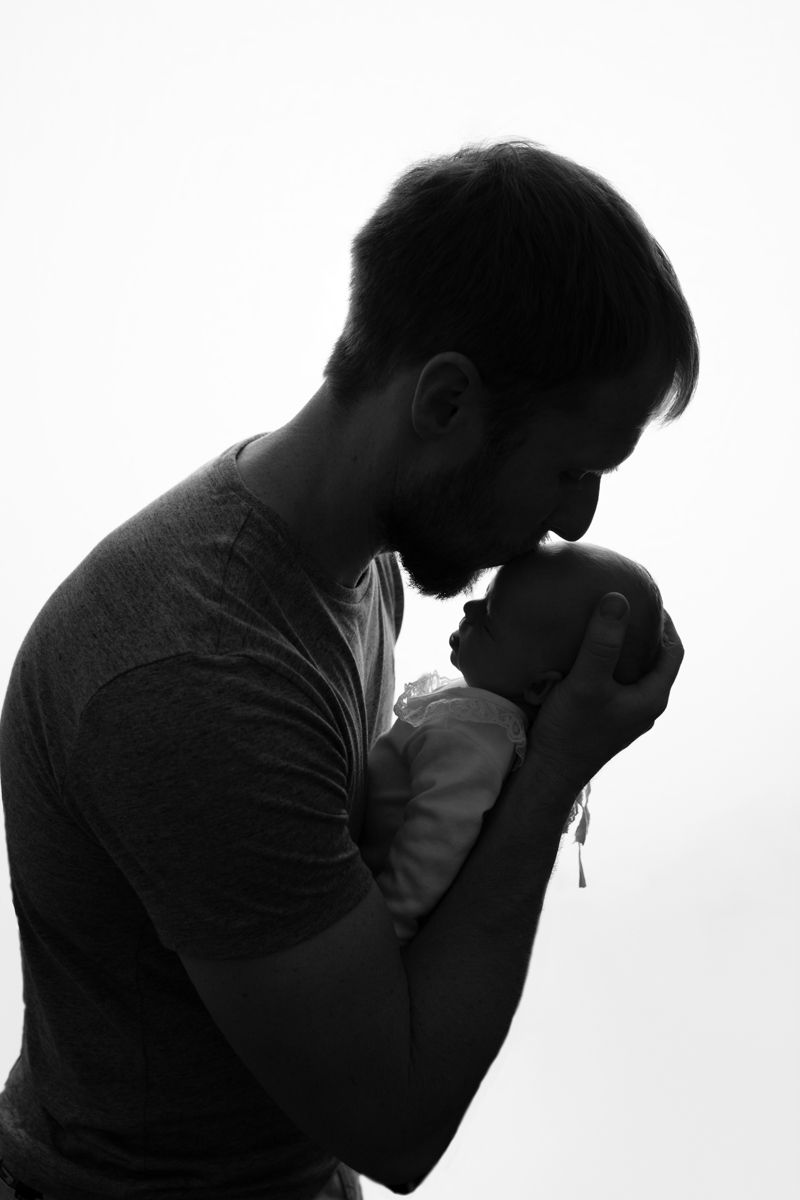 Black and white image of dad and newborn baby girl silhouetted.  Dad is kissing baby's head.