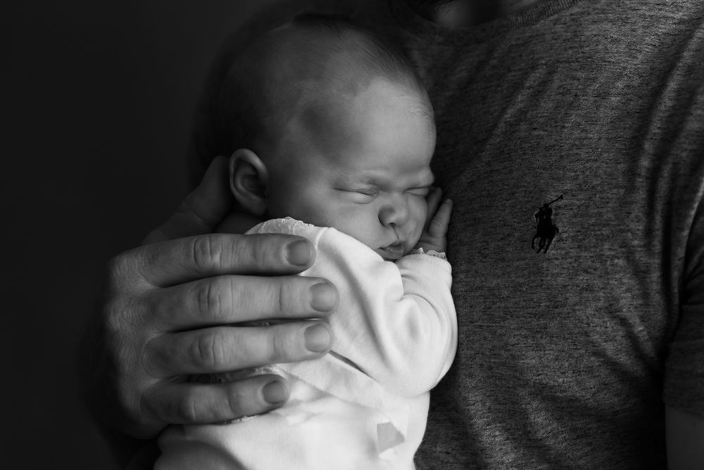 Black and white image of newborn baby girl being held to dad's chest.