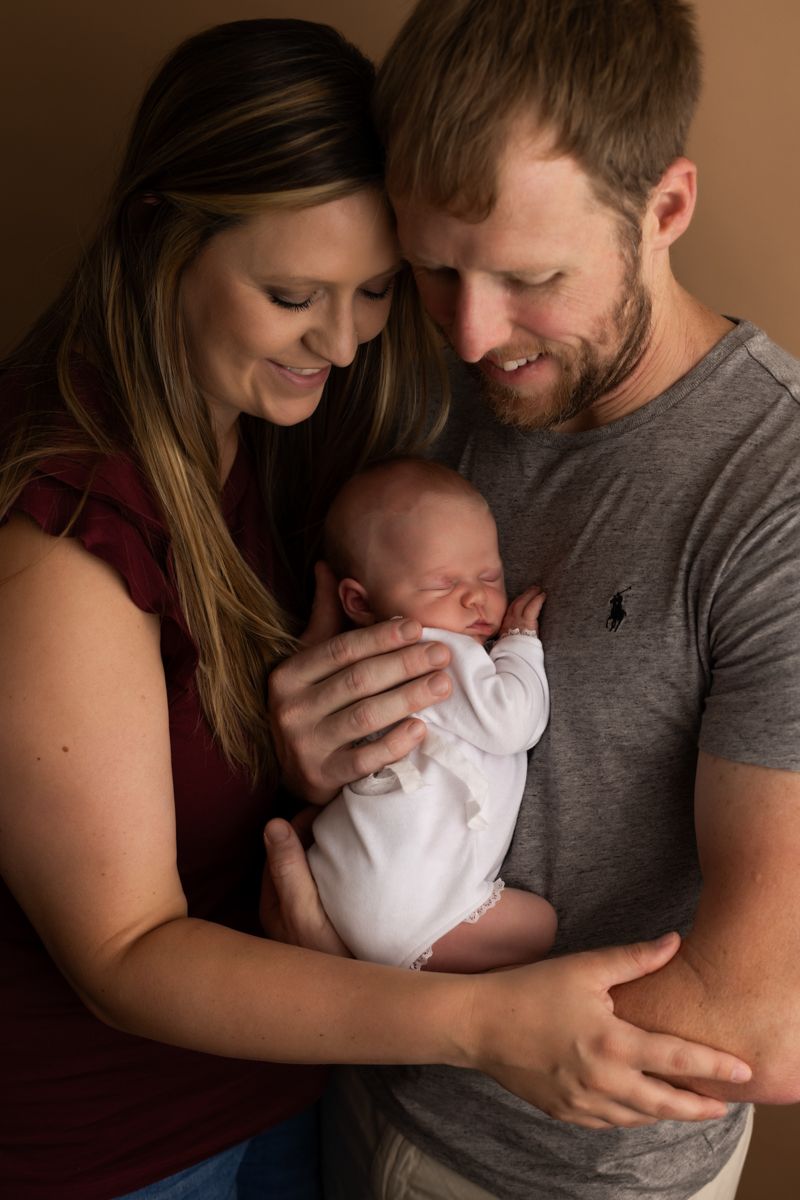 Newborn baby girl being held to dad's chest with both mom and dad smiling down at her.