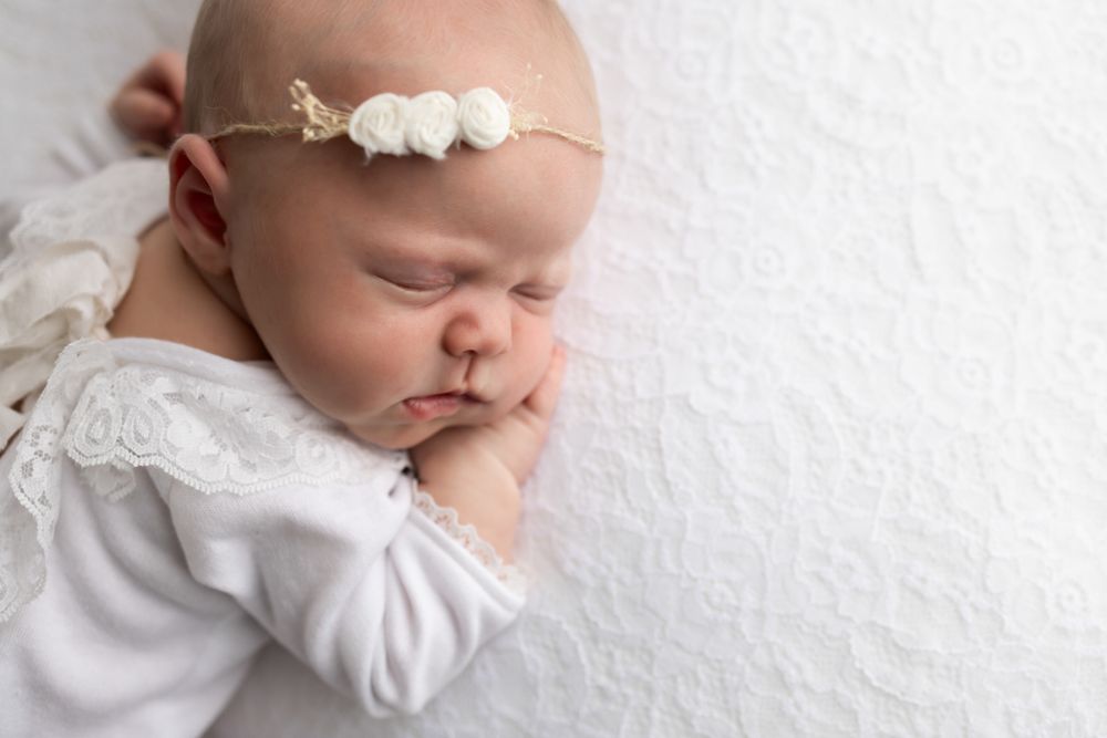 Newborn baby girl in white outfit with floral headband.  Close up of her facial features.