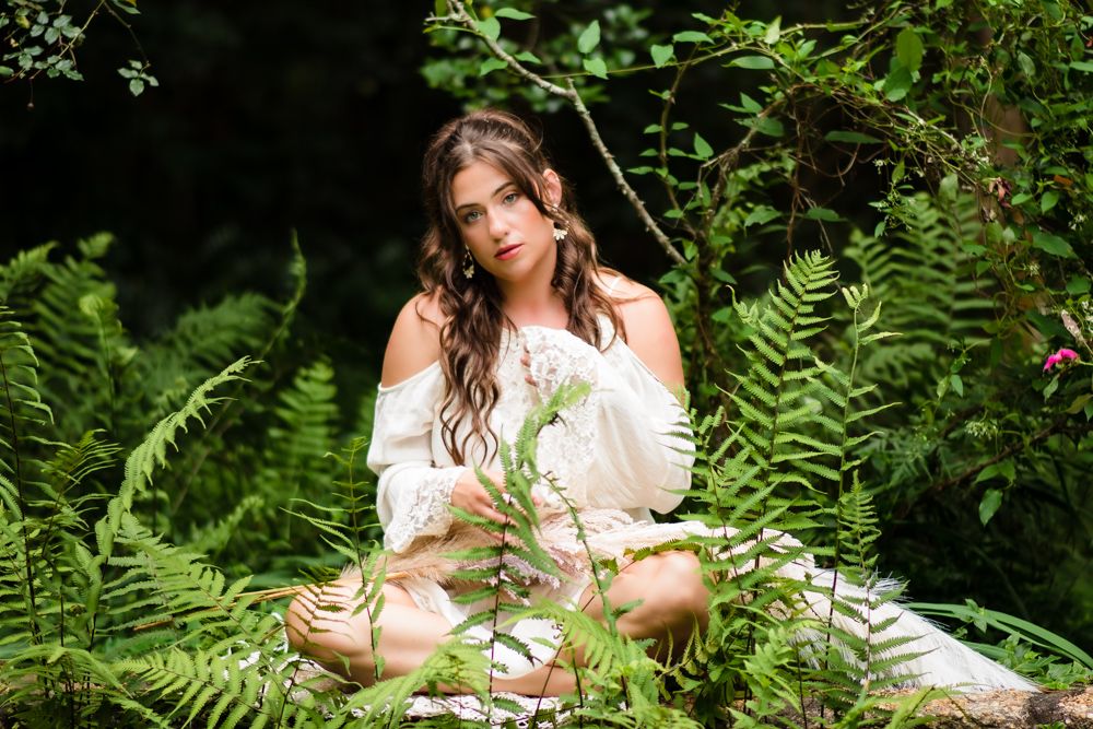 Beautiful woman sitting on a brick wall covered with ferns, showcasing a natural and elegant portrait