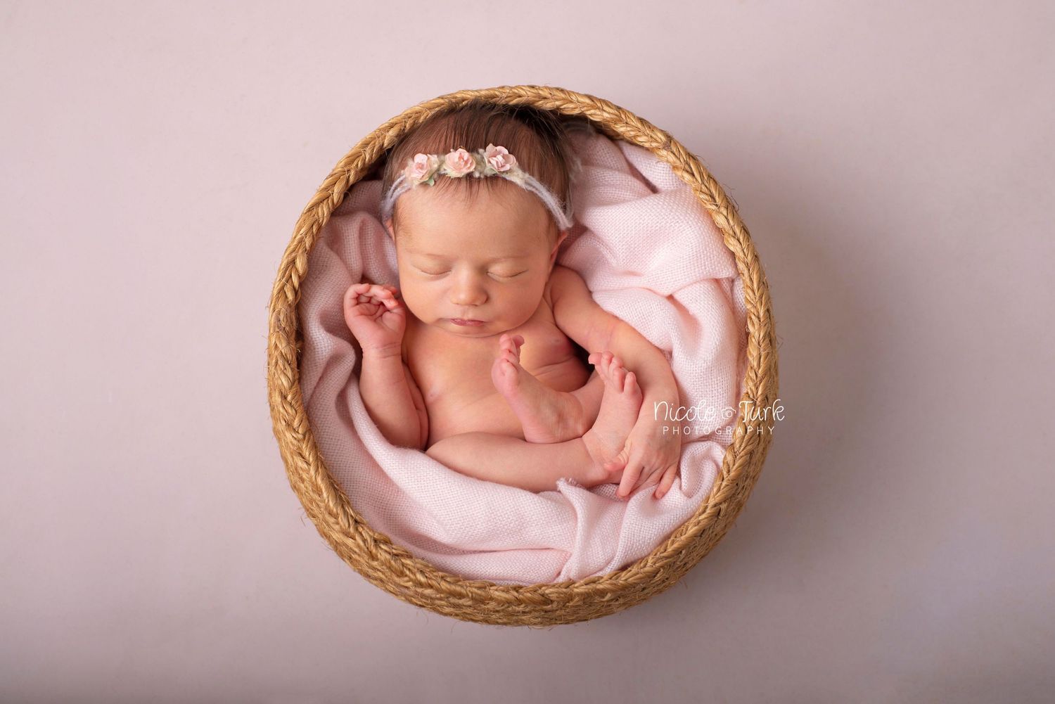 take from above newborn baby on her back curled up in simple woven basket in pink blanket