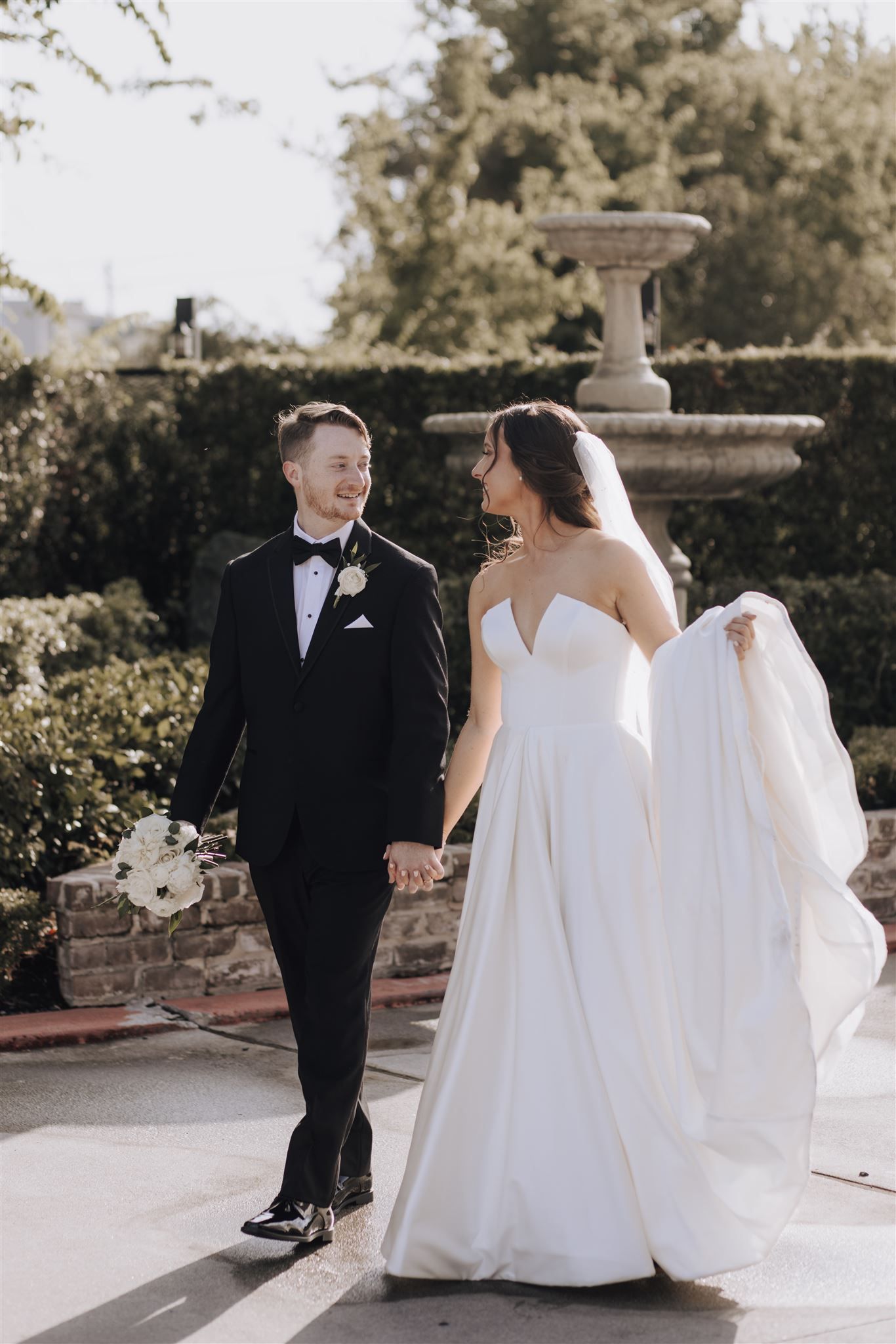 A wedding couple poses together near an elegant garden fountain.