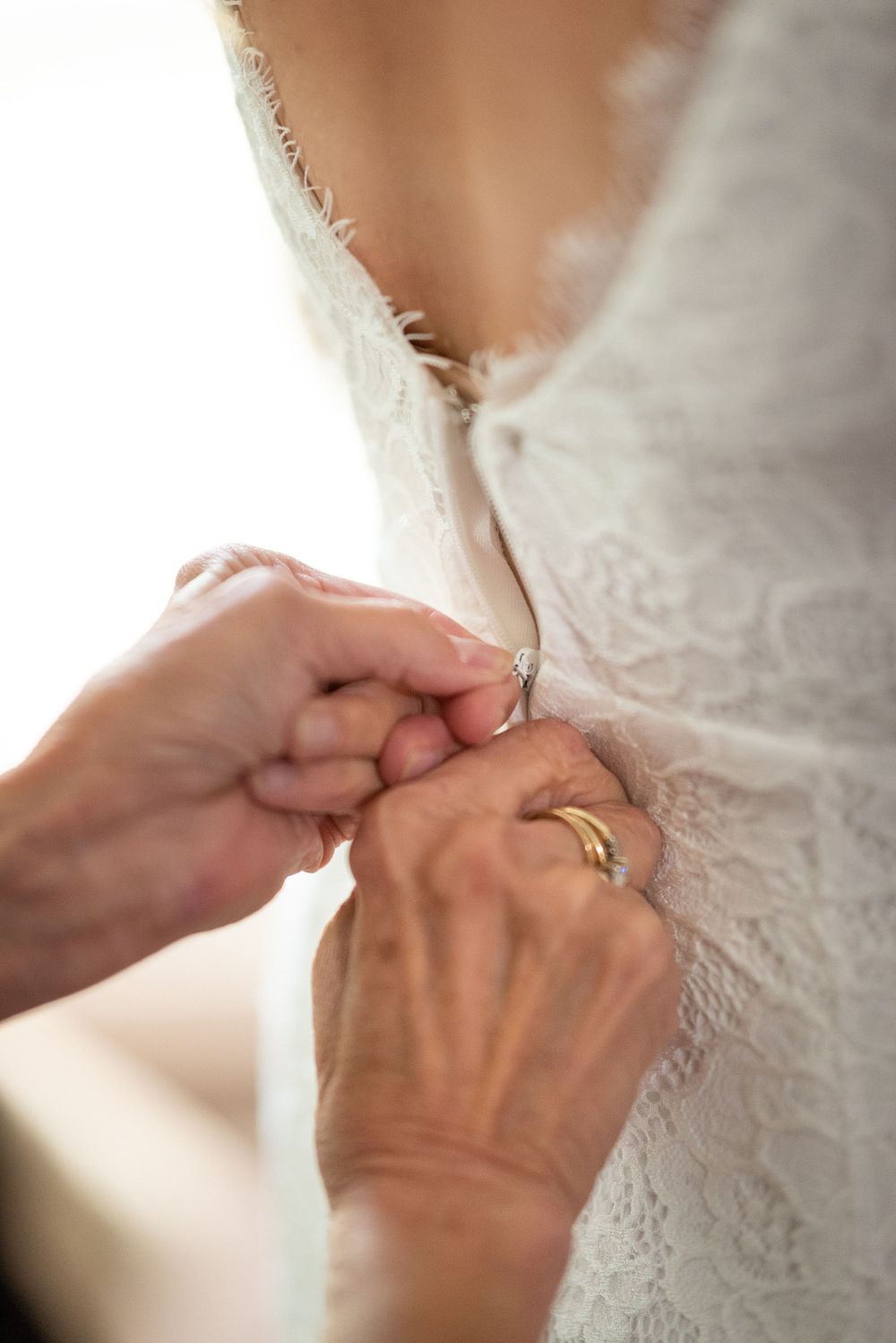 Detailed shot of hands buttoning up the back of an intricate white lace wedding dress.