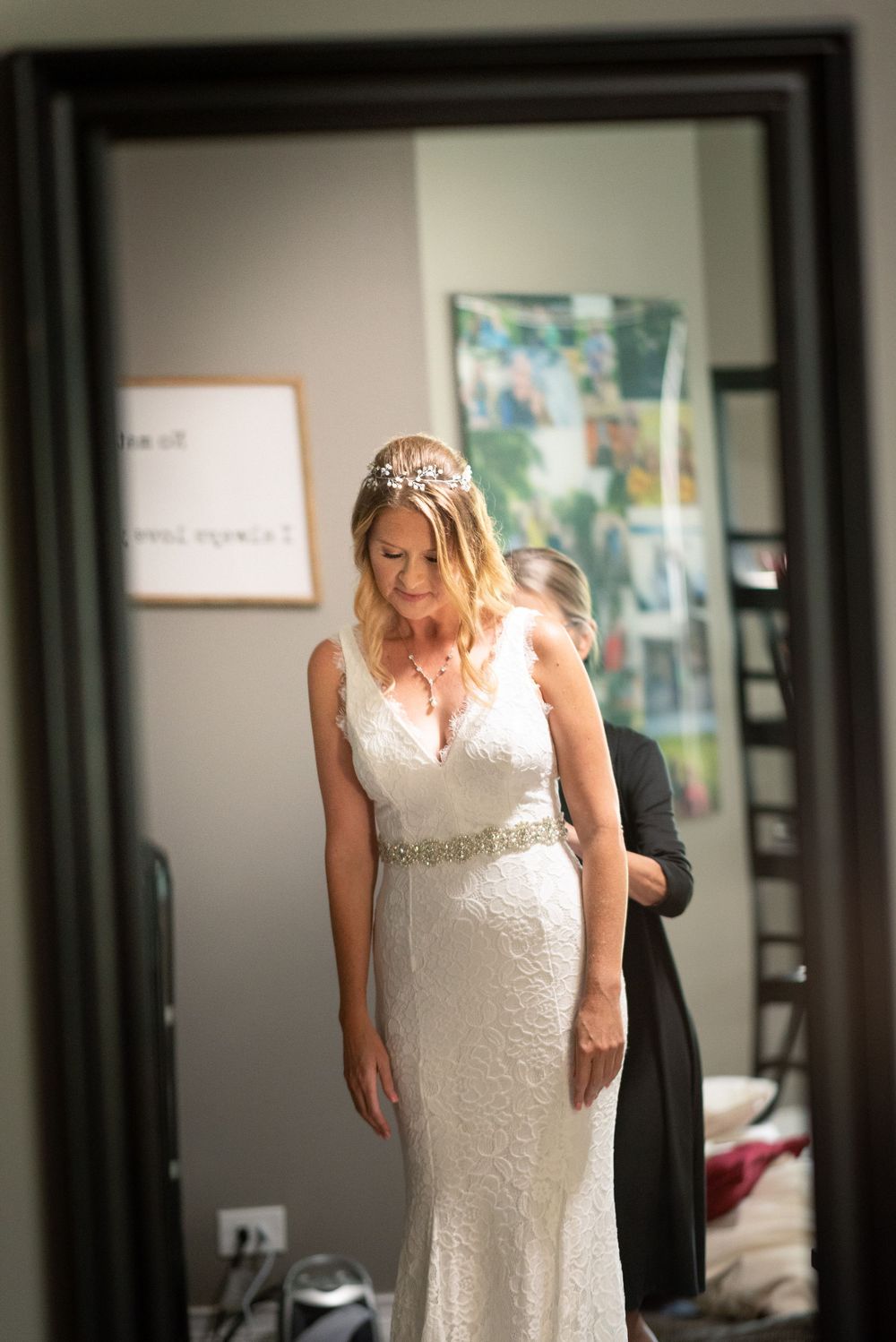 Bride in a fitted white lace wedding dress looks down while standing in front of a mirror.
