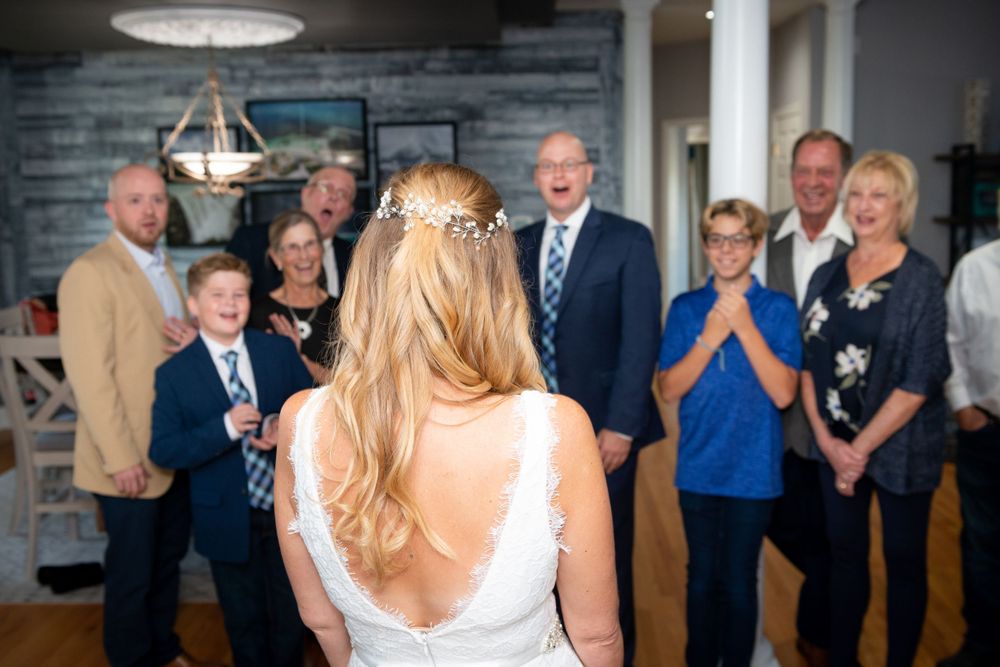 Bride in white dress reveals her gown to family members in a living room setting.