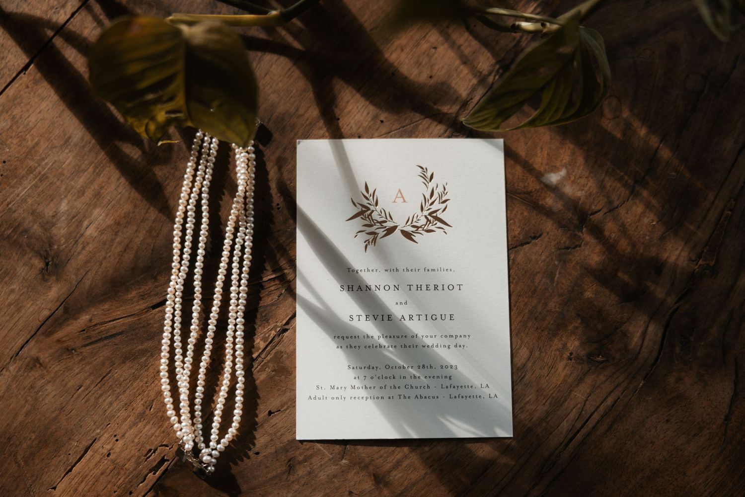 Wedding invitations and pearl necklace arranged on rustic wooden surface with dramatic lighting.