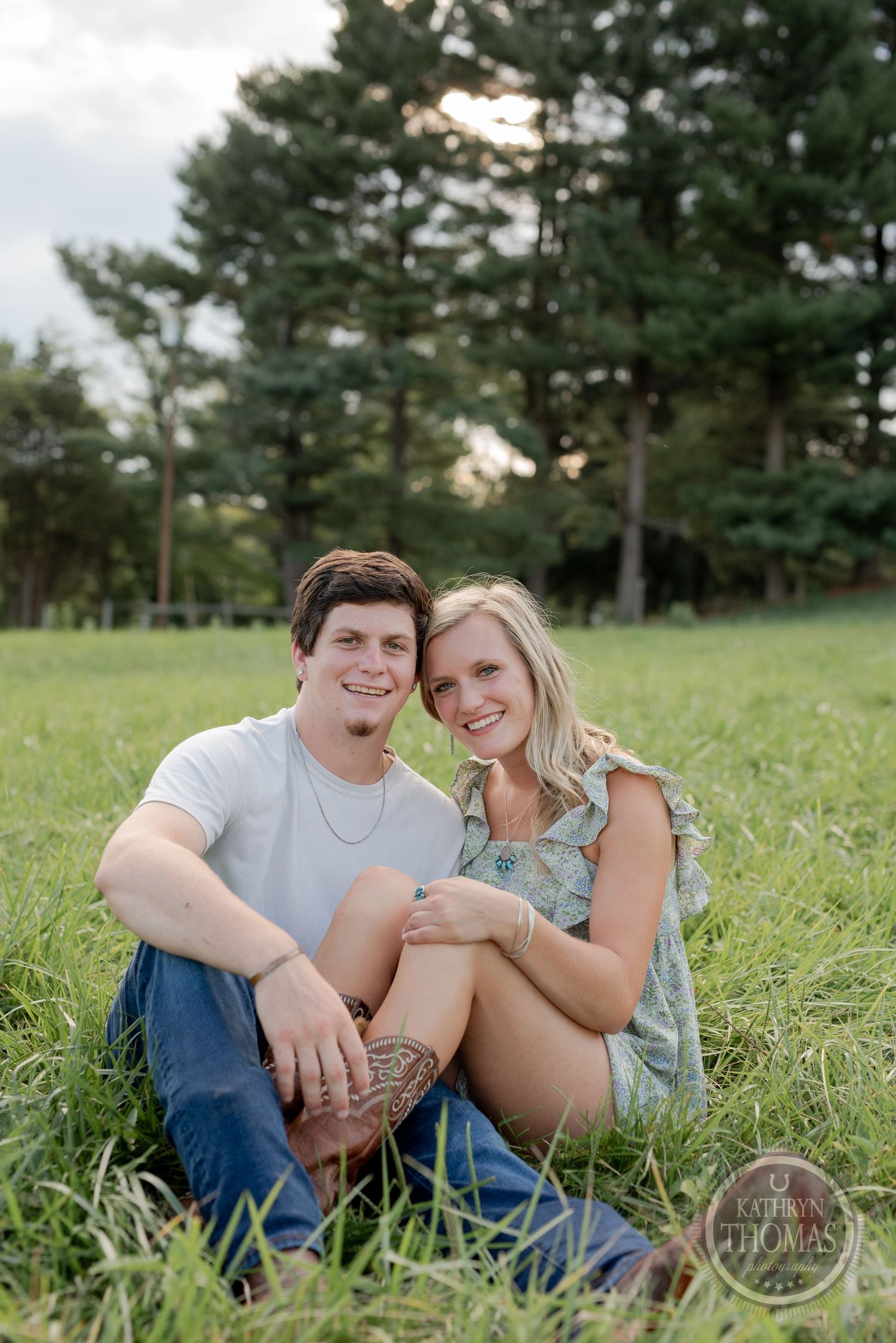 Couple sits together on grassy hillside during summer photoshoot.
