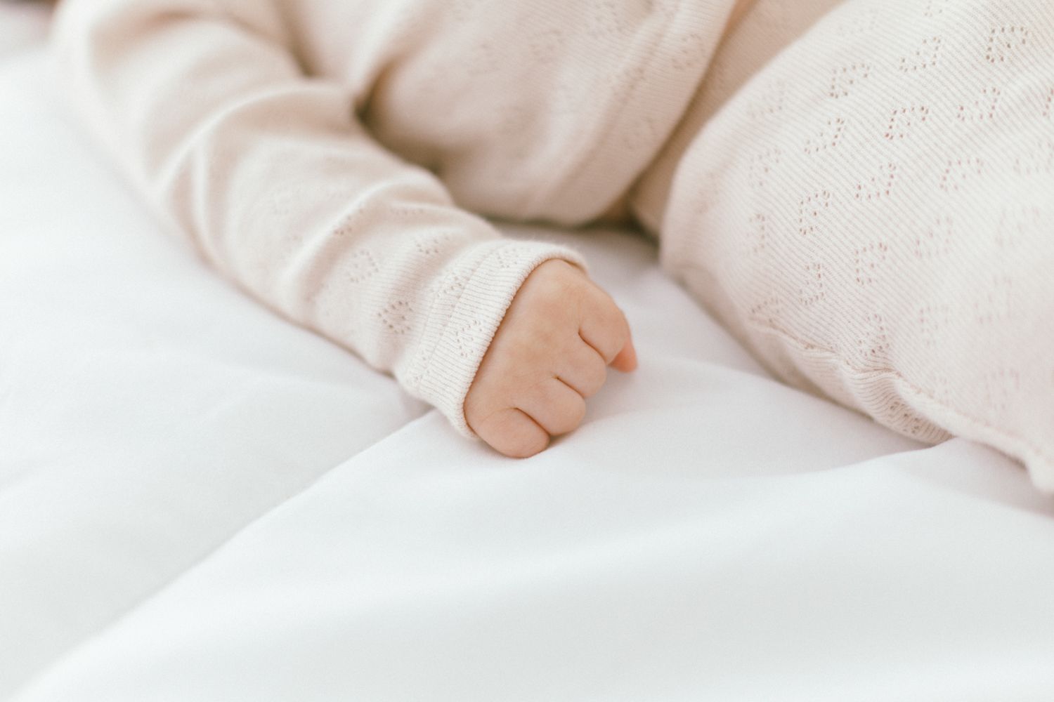 Close-up of tiny baby hand against white bedding.